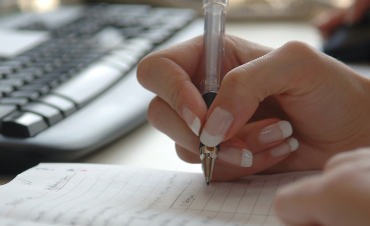 close up of a hand holding a pen and writing on paper