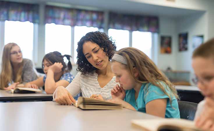 female teacher helping a young student with a reading assignment